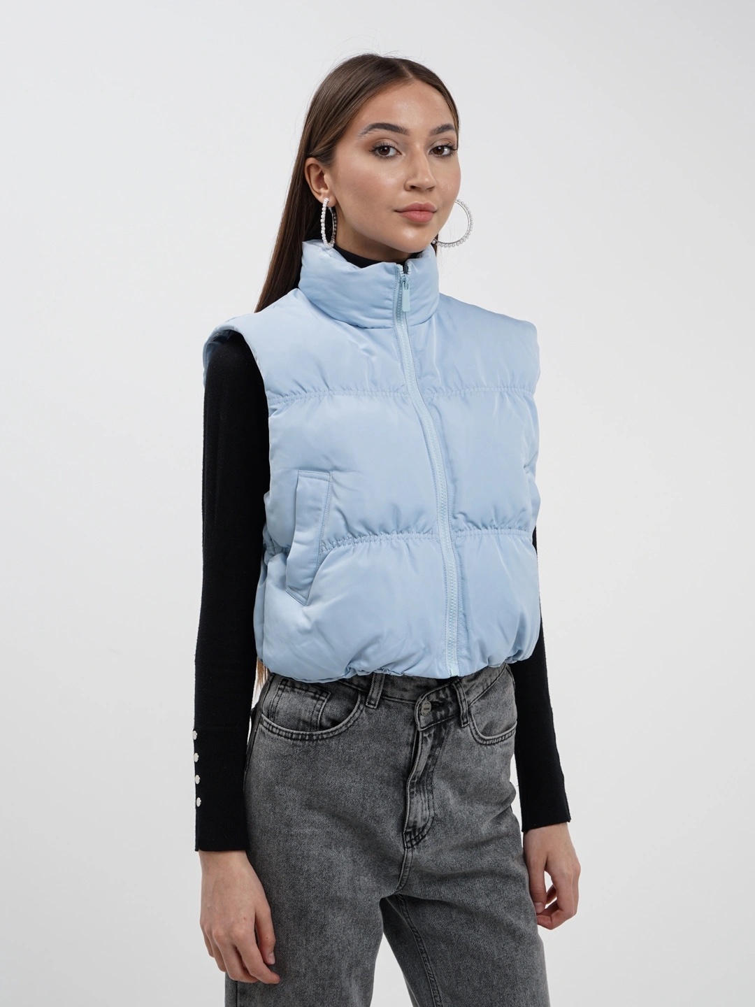 Une veste sans manches matelassée (ou gilet d'hiver) de couleur bleu clair, dotée d'un col cheminée montant, d'une fermeture Éclair à l'avant et de poches latérales