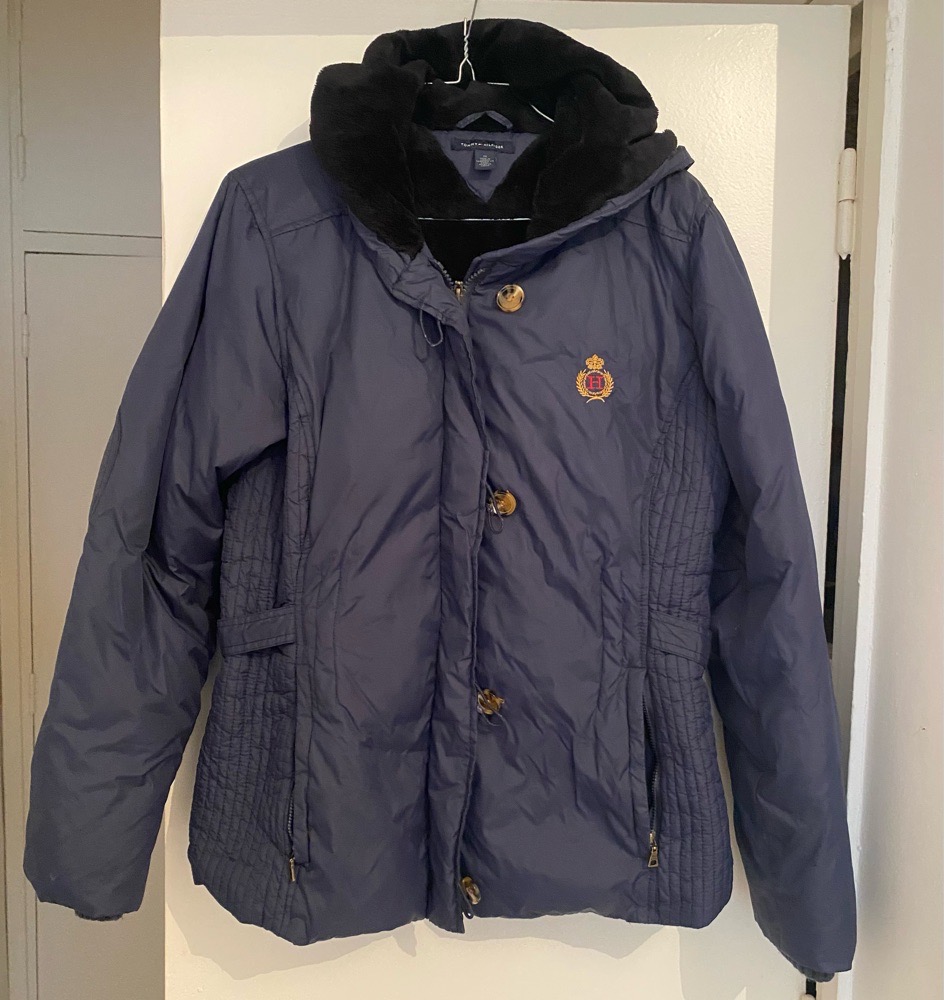 Doudoune Tommy Hilfiger bleu marine avec un col en fausse fourrure noire et un écusson brodé sur la poitrine.