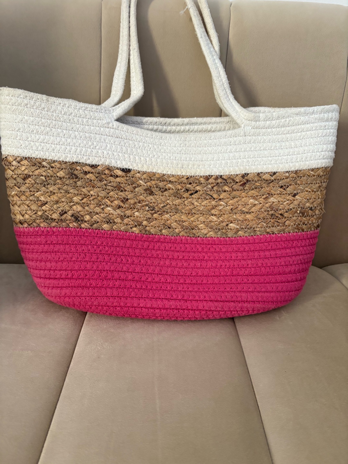 Sac en paille tressée présente un design à rayures horizontales comprenant des bandes blanches, naturelles et fuchsia