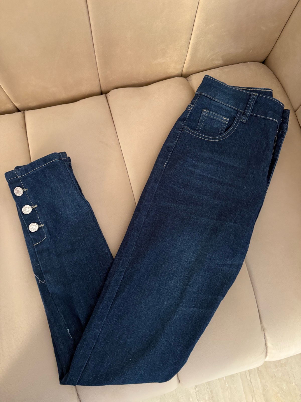 Jeans skinny bleu foncé à taille haute avec des boutons argentés décoratifs.