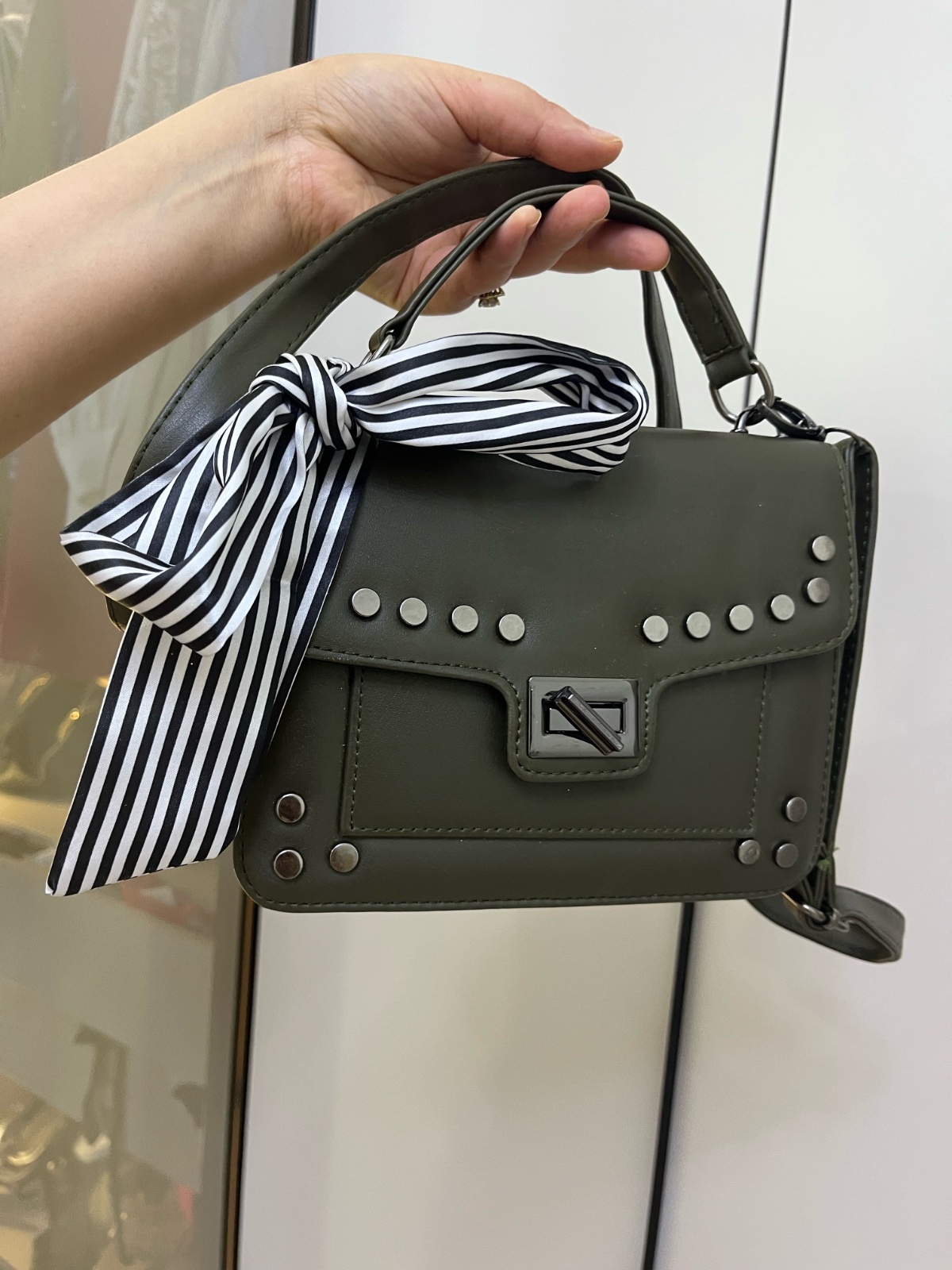 Sac bandoulière de la marque Stradivarius se distingue par ses détails en clous argentés et son foulard rayé noir et blanc attaché à la poignée