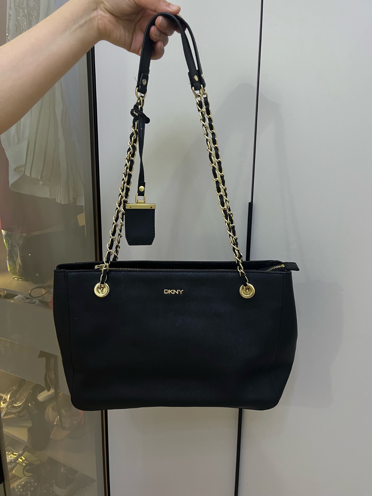Sac est un cabas DKNY en cuir saffiano noir avec des anses en chaîne dorée