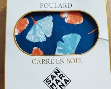 Ce foulard est un carré en soie de la marque San Marina, orné d'un motif de feuilles de ginkgo biloba bleu clair et orange sur un fond bleu marine