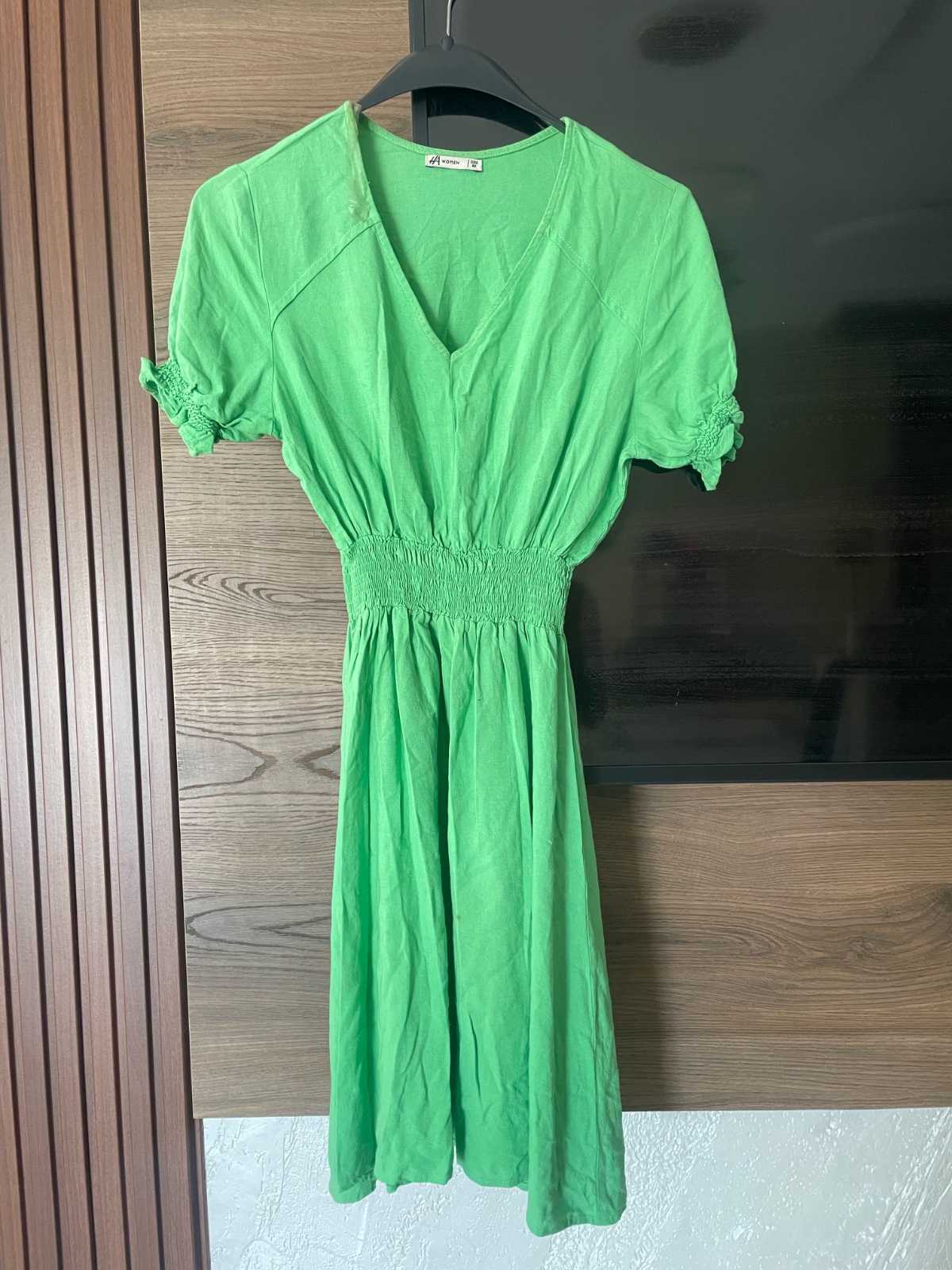 Robe d'été verte et lumineuse, caractérisée par un col en V ainsi qu'une taille et des manches froncées et élastiques.