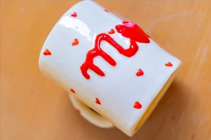 Une tasse en céramique blanche personnalisée avec des motifs de petits cœurs rouges et une inscription en rouge. 