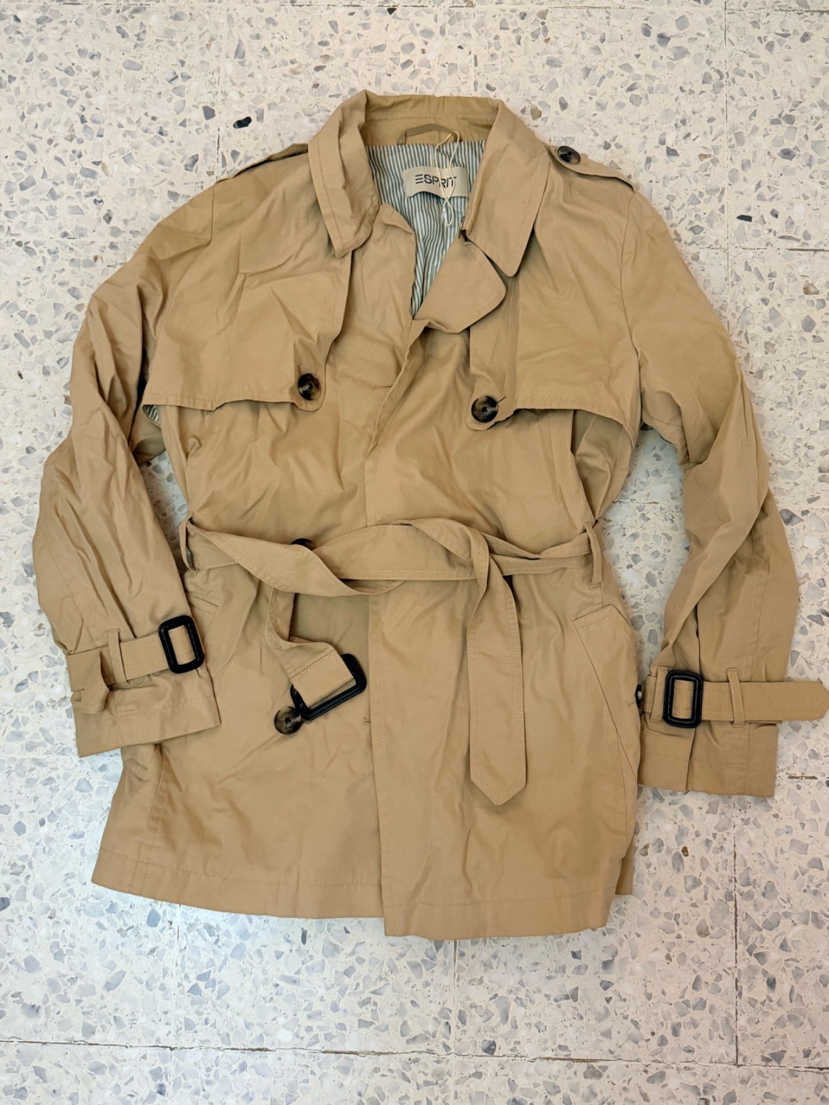 Trench-coat court beige de la marque Esprit doté d'une ceinture à boucle et d'une doublure rayée.