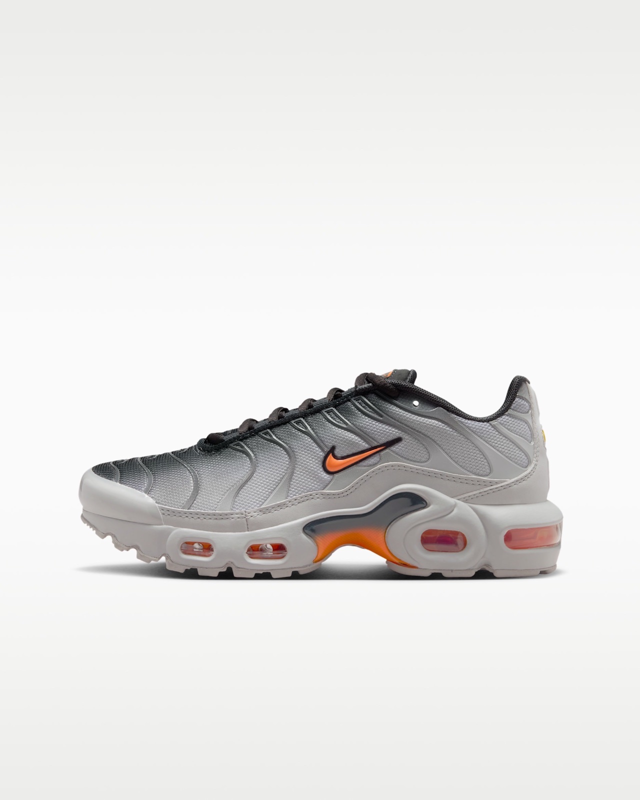 Baskets Nike Air Max Plus (ou TN) en coloris gris clair et accents orange (teinte Light Smoke Grey / Hot Curry), caractérisée par sa cage en plastique ondulée et ses unités d'amorti Air Max visibles sur la semelle Pointure 43
