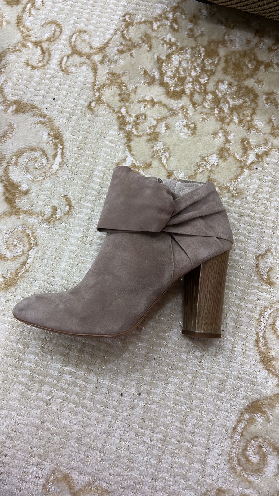 Une bottine en daim taupe à bout pointu présente un talon bloc en bois et un détail de nœud à revers.
