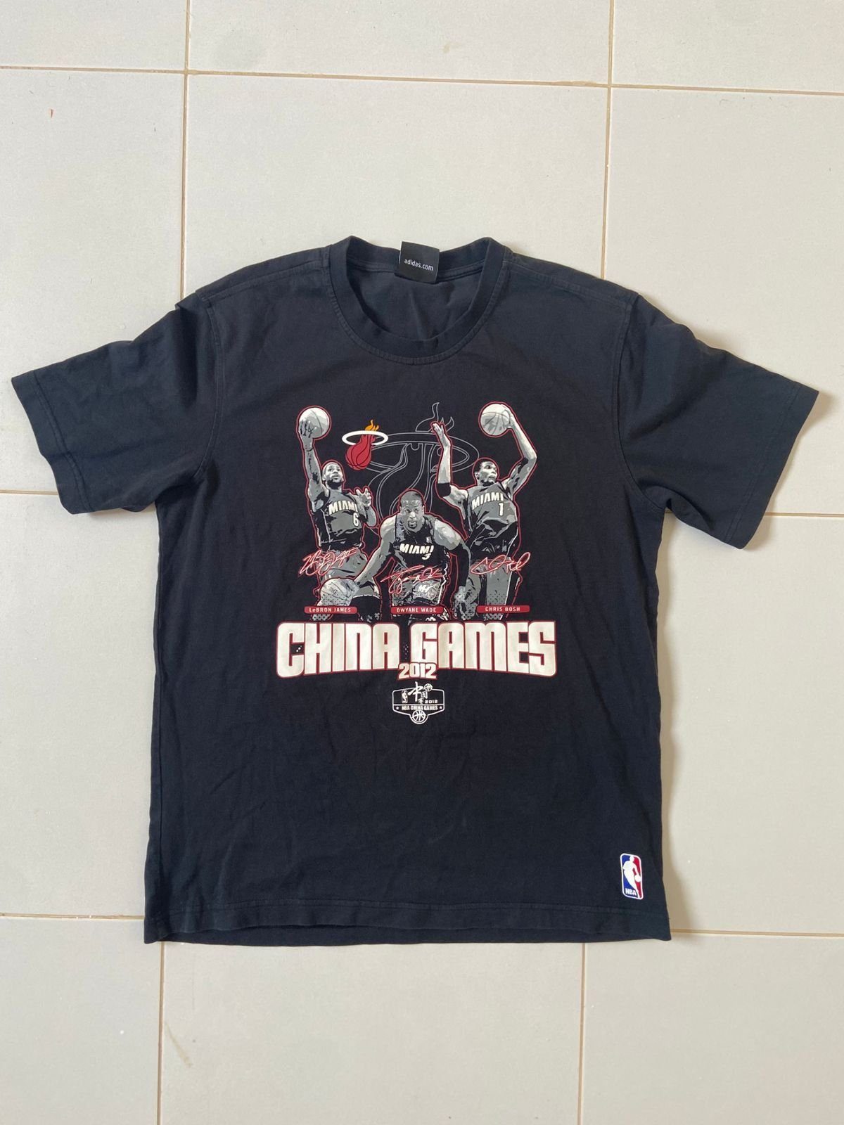 T-shirt noir est un modèle vintage de la marque Adidas commémorant les « China Games 2012 » du Miami Heat, avec les illustrations et signatures de LeBron James, Dwyane Wade et Chris Bosh